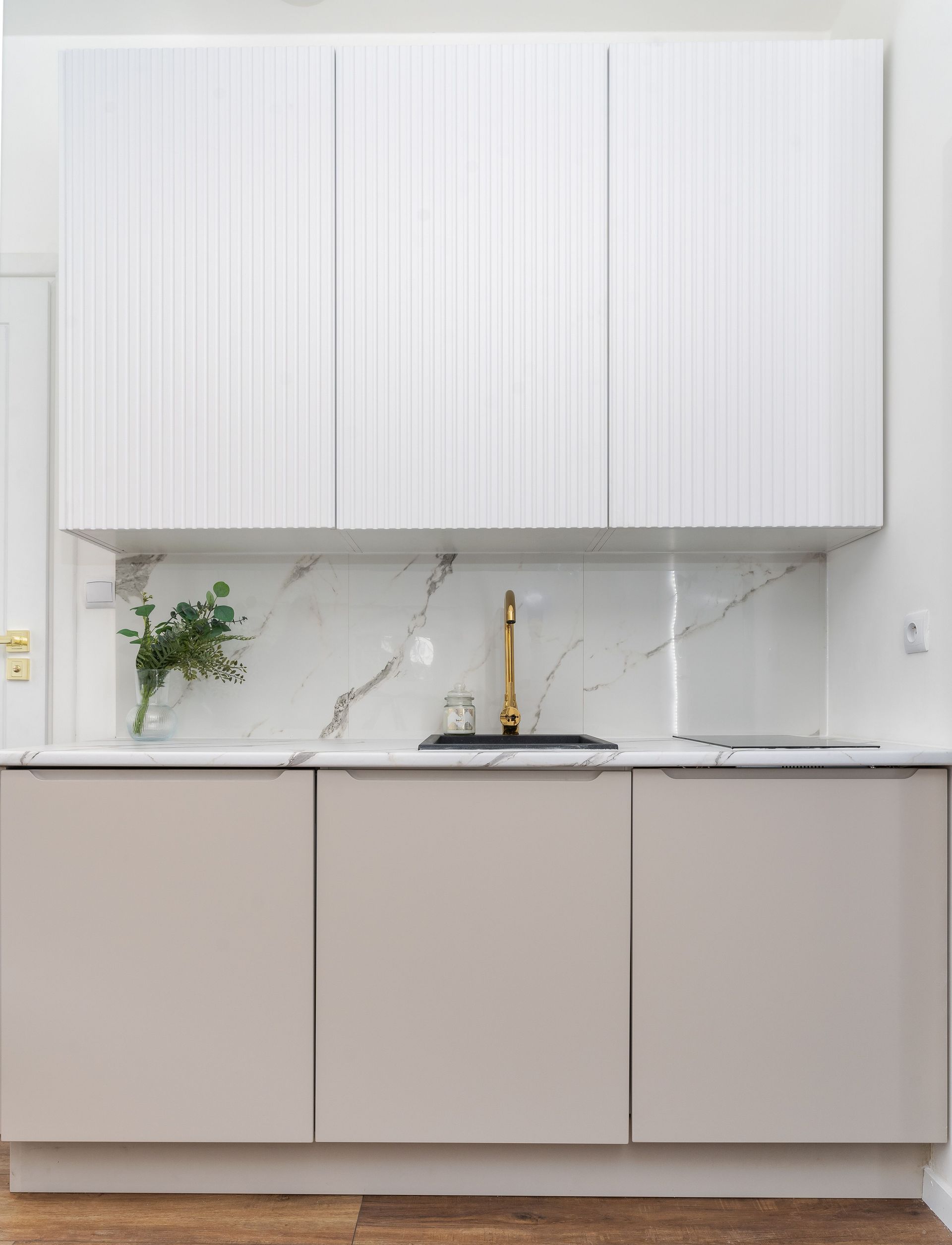 A luxurious minimalist kitchen features marble backsplash and golden faucet.
