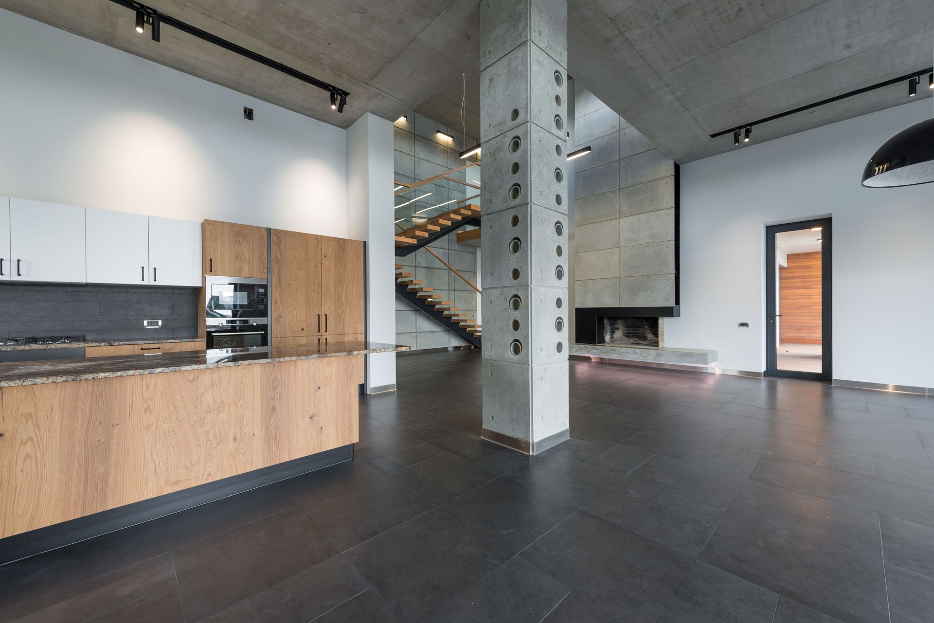 Spacious lobby with marching stairs and wooden kitchen furniture in corner near column